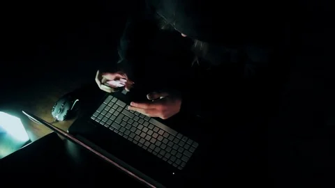 Hacker in hood cracking code using laptop  from his dark hacker room. Stock Footage 73810927