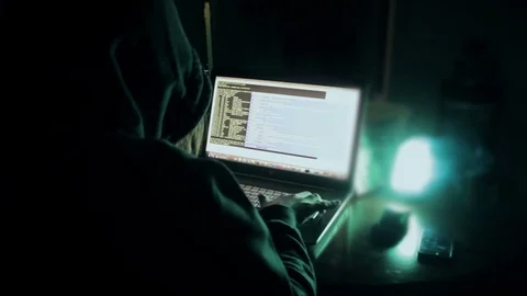 Hacker in hood cracking code using laptop  from his dark hacker room. Stock Footage 73810976