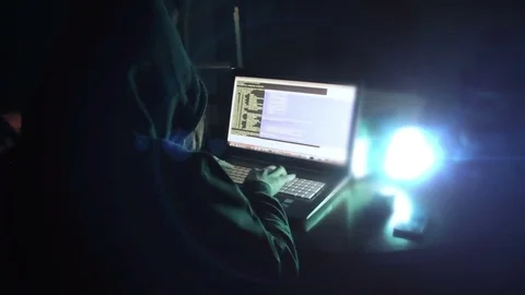 Hacker in hood cracking code using laptop  from his dark hacker room. Stock Footage 73811043