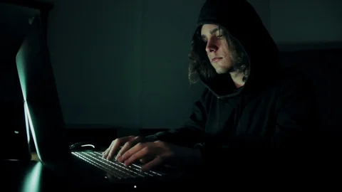 Hacker in hood cracking code using laptop  from his dark hacker room. Stock Footage 73811056