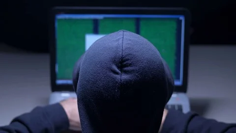 Hacker in hood cracking code using laptop in a room Stock Footage 83712694