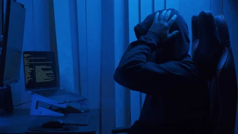 Hacker in hood cracking code using laptop from his dark hacker room Stock Footage 235762150