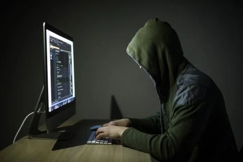 A hacker in a hood on a dark background hacking computer networks in dark roo 스톡 사진