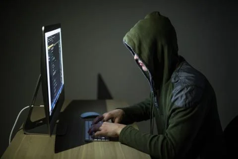 A hacker in a hood on a dark background hacking computer networks in dark roo Foto stock