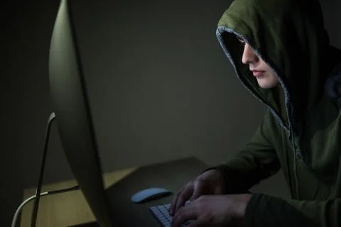 A hacker in a hood on a dark background hacking computer networks in dark roo Stock Photos