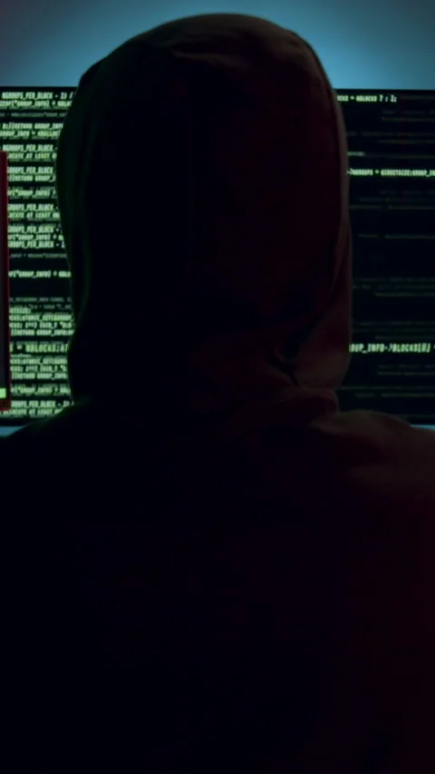 Hacker with a hood on his head in front of large computer towers, image from Video stock 313925803
