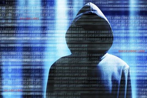 A hacker with a hood over a screen with binary code 스톡 사진
