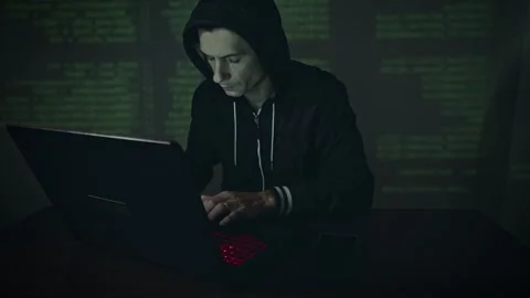 Hacker in hood typing program code while committing a cybercrime hacking Stock Footage 283996455