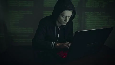 Hacker in hood typing program code while committing a cybercrime hacking Stock Footage 283996473