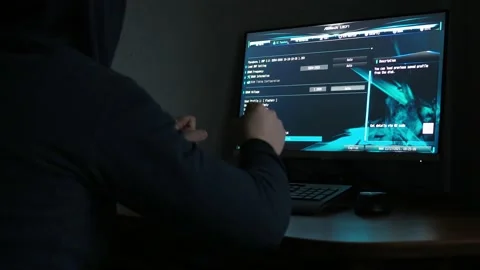 A hacker in a hooded sweatshirt is sitting at a computer in the dark. light from Video stock 166110239
