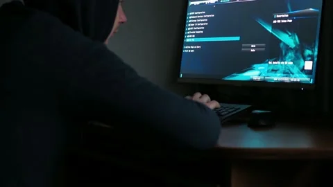A hacker in a hooded sweatshirt is sitting at a computer in the dark. light from Stock Footage 167796677