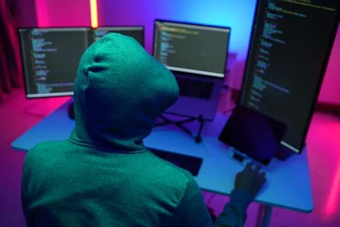 Hacker in Hoodie Coding on Multiple Monitors in Neon Light Stock Photos