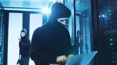 Hacker in hoodie coding program on laptop, gaining access to server cabinet Stock Footage 120694817