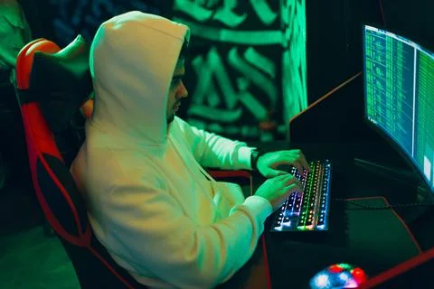 Hacker in hoodie working hacks code site on personal computer with green light Stock Photos