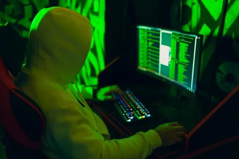 Hacker in hoodie working hacks code site on personal computer with green light Stock Photos