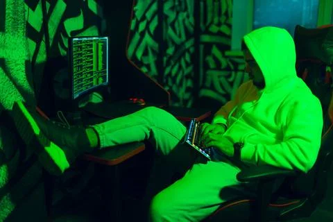Hacker in hoodie working hacks code site on personal computer with green l... 스톡 사진