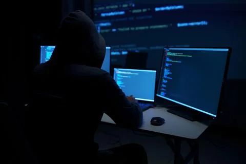 Hacker in Hoodie Working on Multiple Code Monitors 库存照片