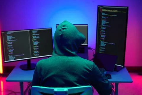 Hacker in Hoodie Working at Multiple Monitors in Neon Light Foto stock