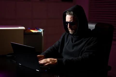Hacker with laptop in a dark office. Anonymous hacker in a hoodie hacking data Stock Photos