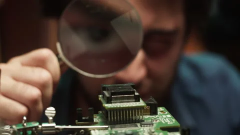 Hacker looking at microchip, using magnifier close-up. Young Spanish man Stock-Footage 164414600