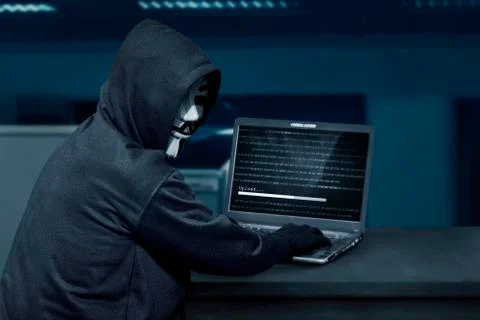 Hacker man wearing mask using laptop to upload computer virus 写真素材