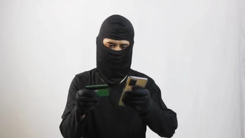Hacker in mask using stolen credit card and phone for cyber crime Stock Footage 319411694