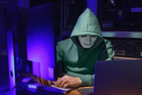 Hacker in mask working with computers in dark room. Cyber attack Stock Photos