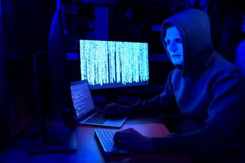 Hacker in mask working with computers in dark room. Cyber attack Stock Photos