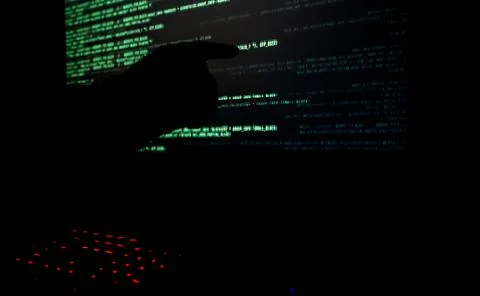 Hacker pointing to code on a computer monitor in a dark room. 스톡 사진