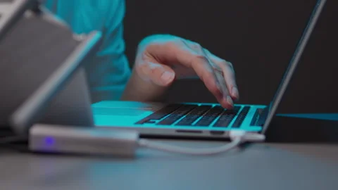 Hacker programming and typing on laptop keyboard in dark room with single light Vidéo 342761564