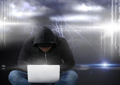 Hacker seated with cross-legged using a laptop in front of storm background Foto stock