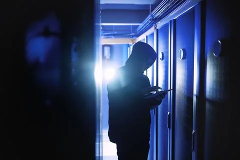 Hacker, tablet and hoodie in server room for cyber crime, phishing and typing Stock Photos