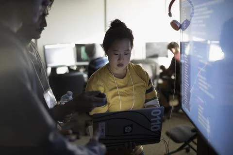 Hacker team coding at laptop and computer monitor at hackathon in dark office 스톡 사진