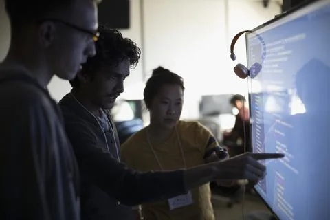 Hacker team discussing coding on computer monitor at hackathon in dark office Foto stock