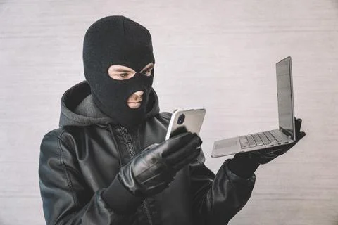 A hacker thief uses a smartphone and laptop to steal money over the Internet. 스톡 사진