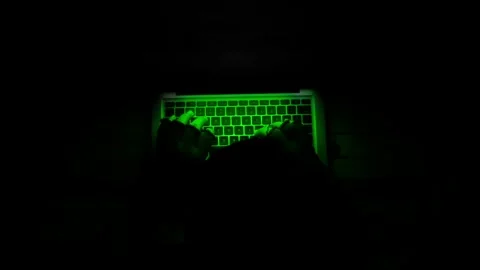 Hacker typing on a glowing green laptop keyboard in dark room. Stock Footage 333032499