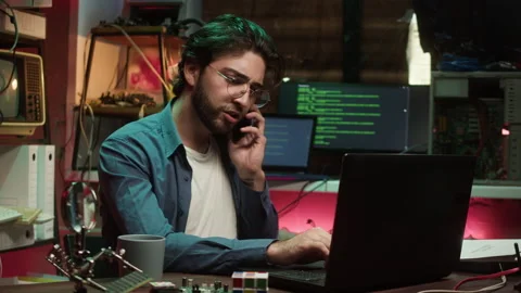 Hacker using laptop and speaking on phone. Young Spanish man developing program Stock-Footage 228685943