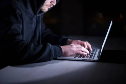 Hacker using laptop computer while working in dark office Young talented h... Stock-Fotos
