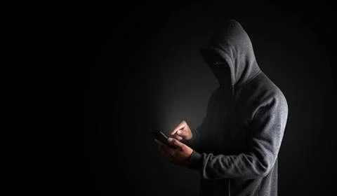 Hacker Using Smartphone. Men in black clothes with hidden face looks Stock Photos