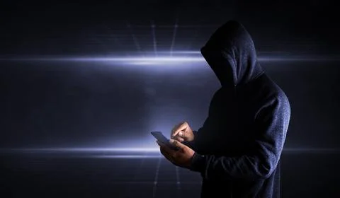 Hacker Using Smartphone. Men in black clothes with hidden face looks at sma.. Stock Photos