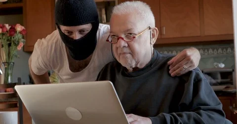 Hacker viewing an unsuspecting older man's private information on his computer Video stock 79804053