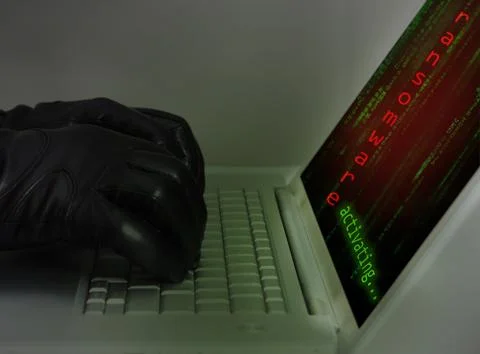 Hacker wearing black gloves using a laptop preparing an attack using ransomwa Stock Photos