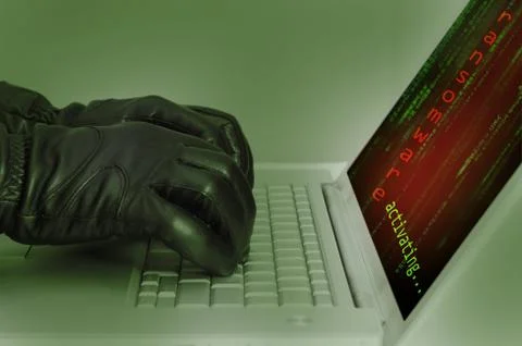 Hacker wearing black gloves using a laptop preparing an attack using ransomwa Stock Photos