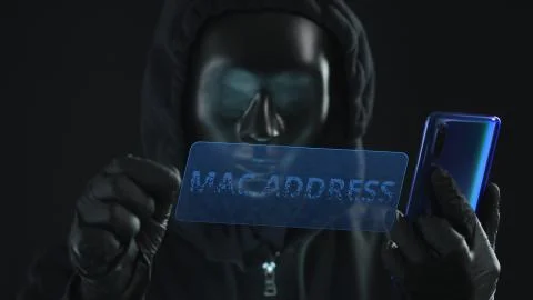 Hacker wearing black mask pulls MAC ADDRESS tab from a smartphone. Hacking Stock Photos