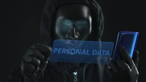 Hacker wearing black mask pulls PERSONAL DATA tab from a smartphone. Hacking Stock Photos