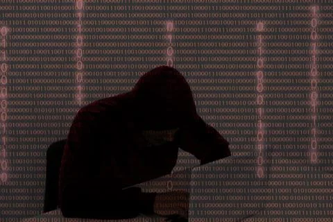 Hacker wearing a hooded top using laptop computer in the dark. The man breaks Foto stock