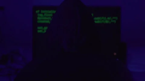 Hacker wearing hoodie codes in the shadows with police lights Stock Footage 262475027