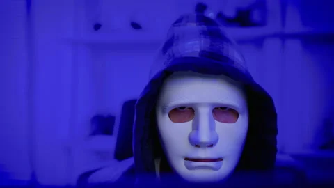 Hacker wearing a white mask is using a computer Stock Footage 234425501