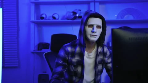 Hacker wearing a white mask is using a computer to steal information Stock Footage 246009570