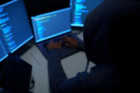 Hacker Working at Multiple Monitors in Dark Room Foto stock